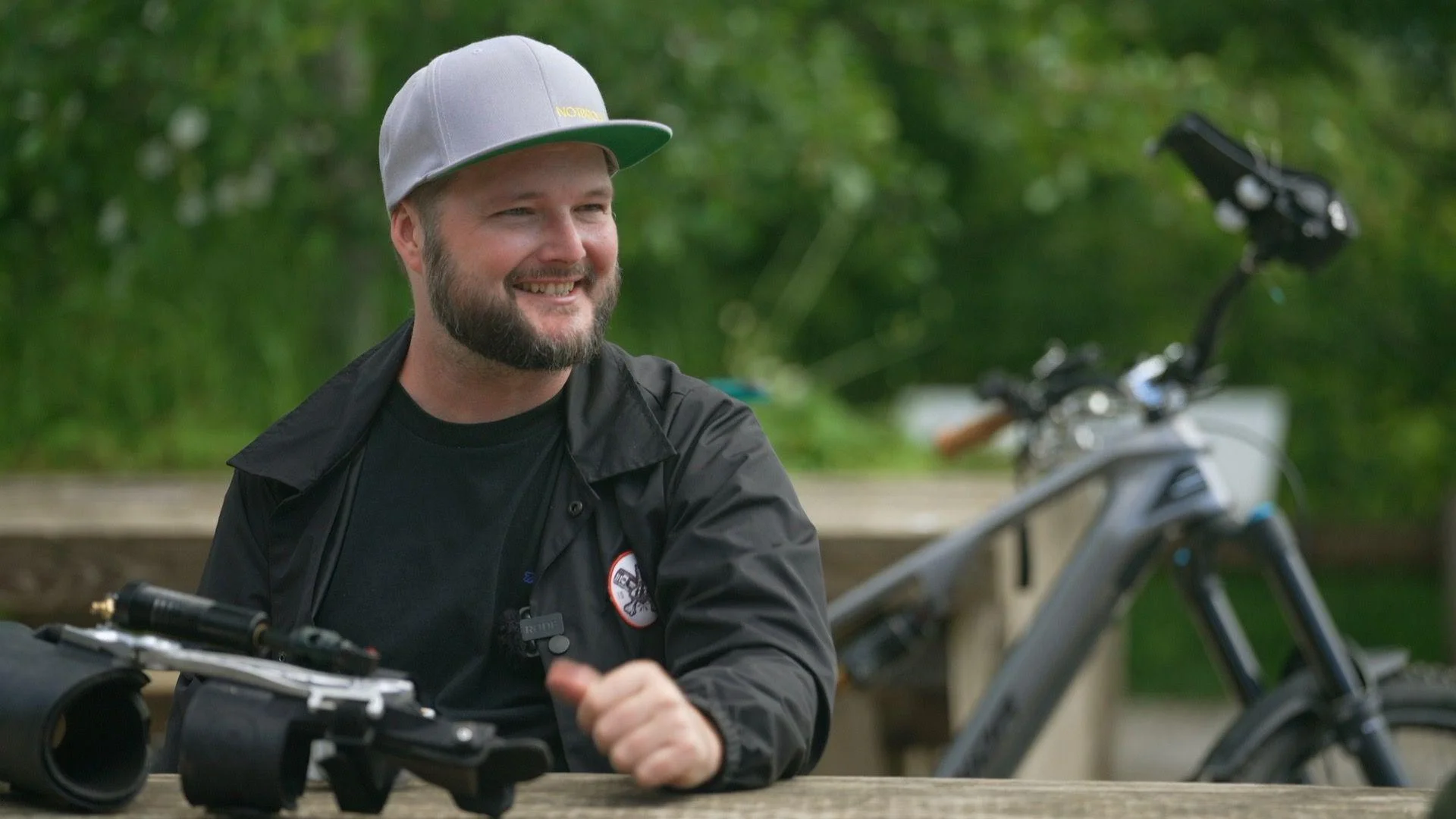 Tom Wheeler sits at a picnic table with his mountain bike behind him.