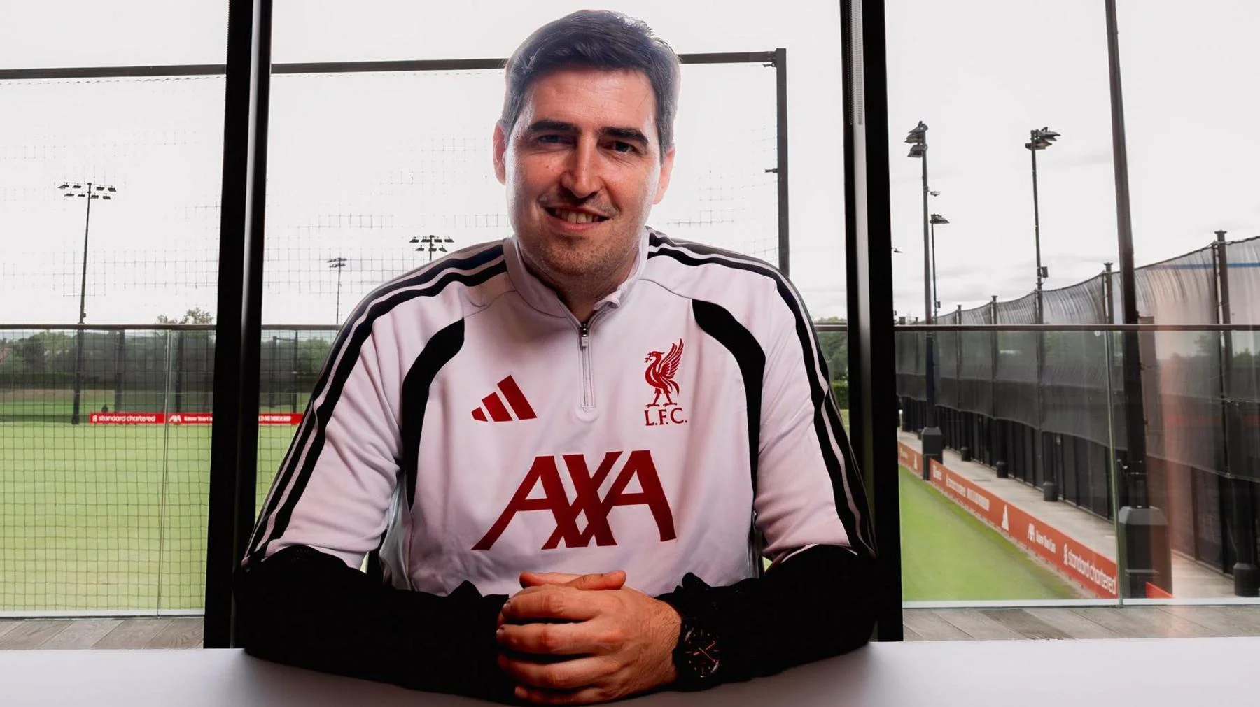 New Liverpool manager Andoni Iraola in white and black club training kit with red lettering, sitting at a table at the club's training ground