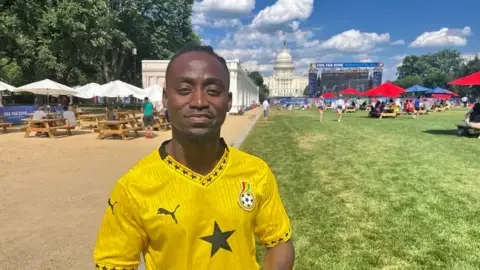 Christian Boateng stands posing in a football jersey. Behind him you can see the US Capitol and FIFA World Cup celebrations