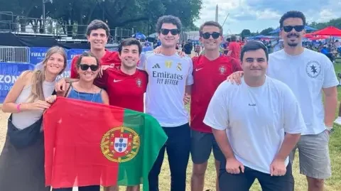 A group of eight Portuguese fans fans pose for a photo. The flag of Portugal is in the left of the photo.