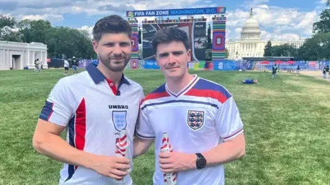 Harry Beckley (left) and Jason Barnes pose for a photo. They are wearing England's white team jersey and the US Capitol is behind them. A large screen at the Fifa Fan Zone in Washington DC is also behind them.