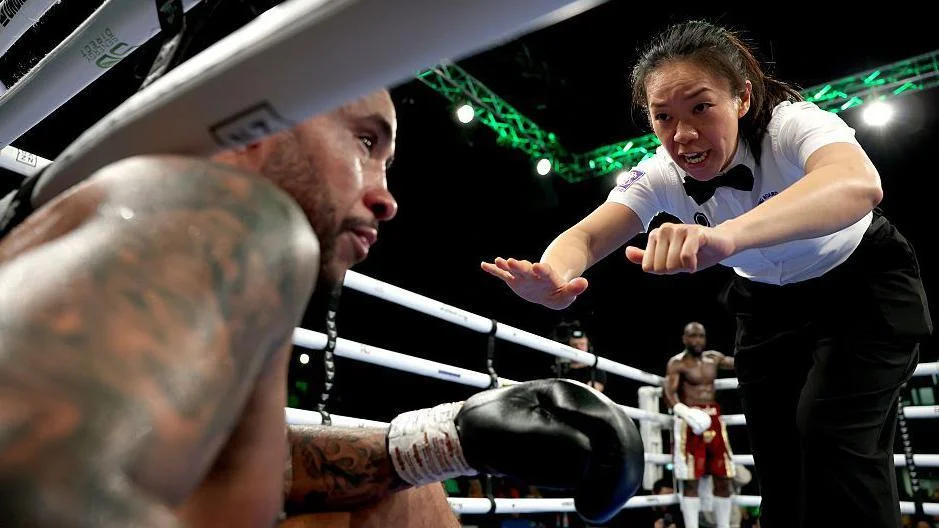 Amy Pu counts with her fingers as Grant Dennis sits on the floor in the ring