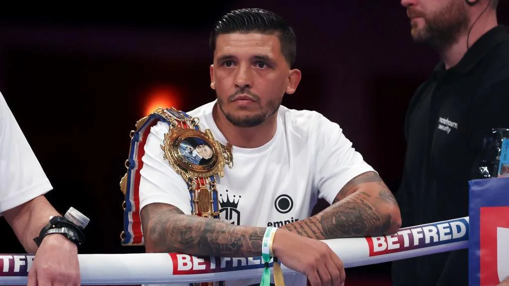Lee Selby wears a white T-shirt with a Lonsdale belt over his shoulder, leaning on the ropes from the ring apron before a Joe Cordina fight in Cardiff